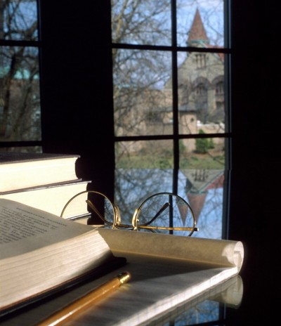 Image of a desk with a notebook and pencil with window overlooking campus in the background.