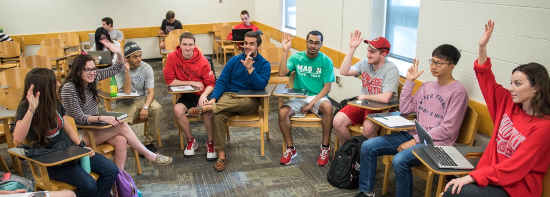 An image of students raising their hands during a Political Science class
