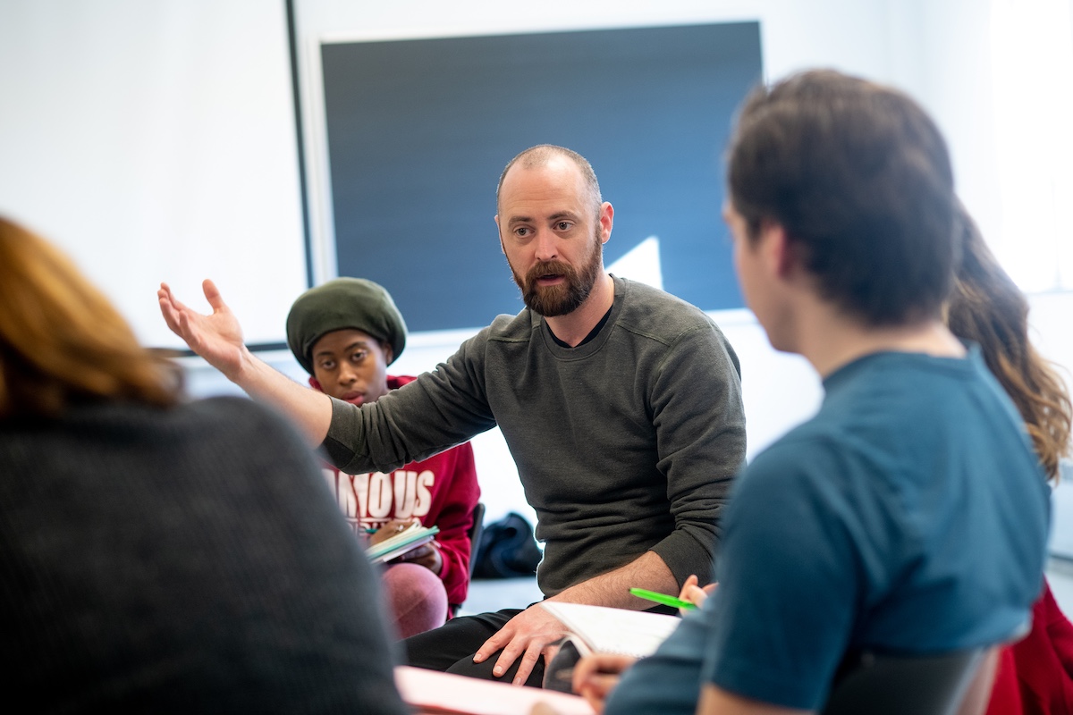 A faculty member sits and talks with a class of students.