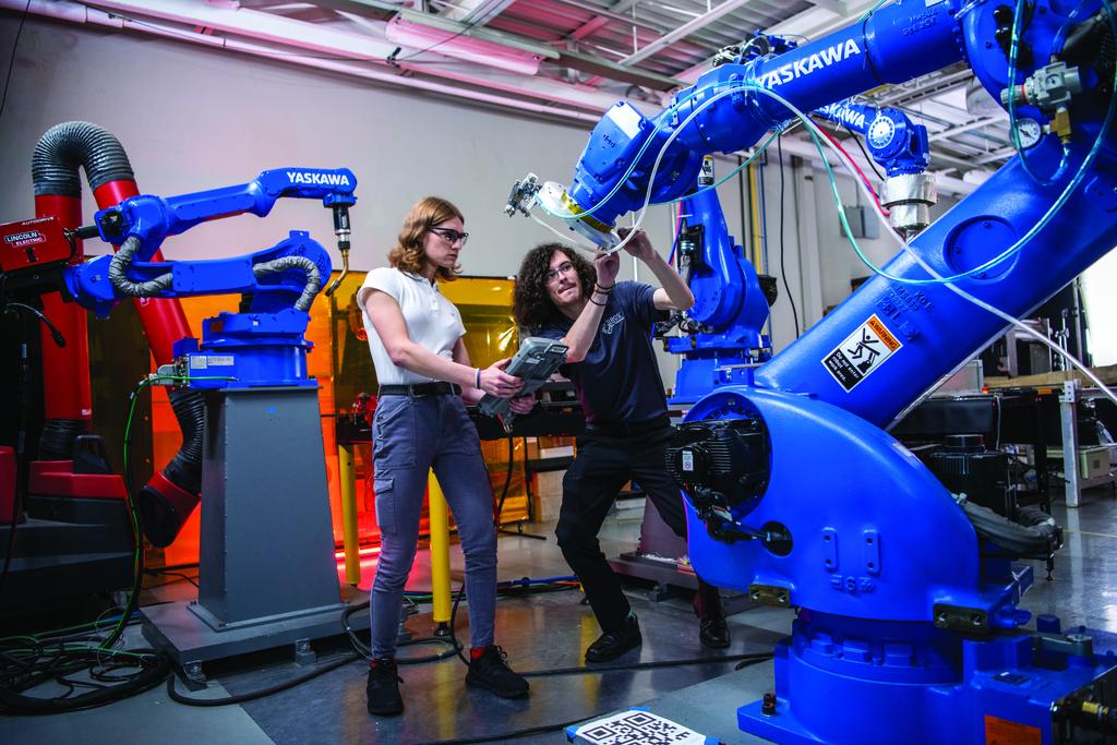 Two students work with a very large robotic arm.