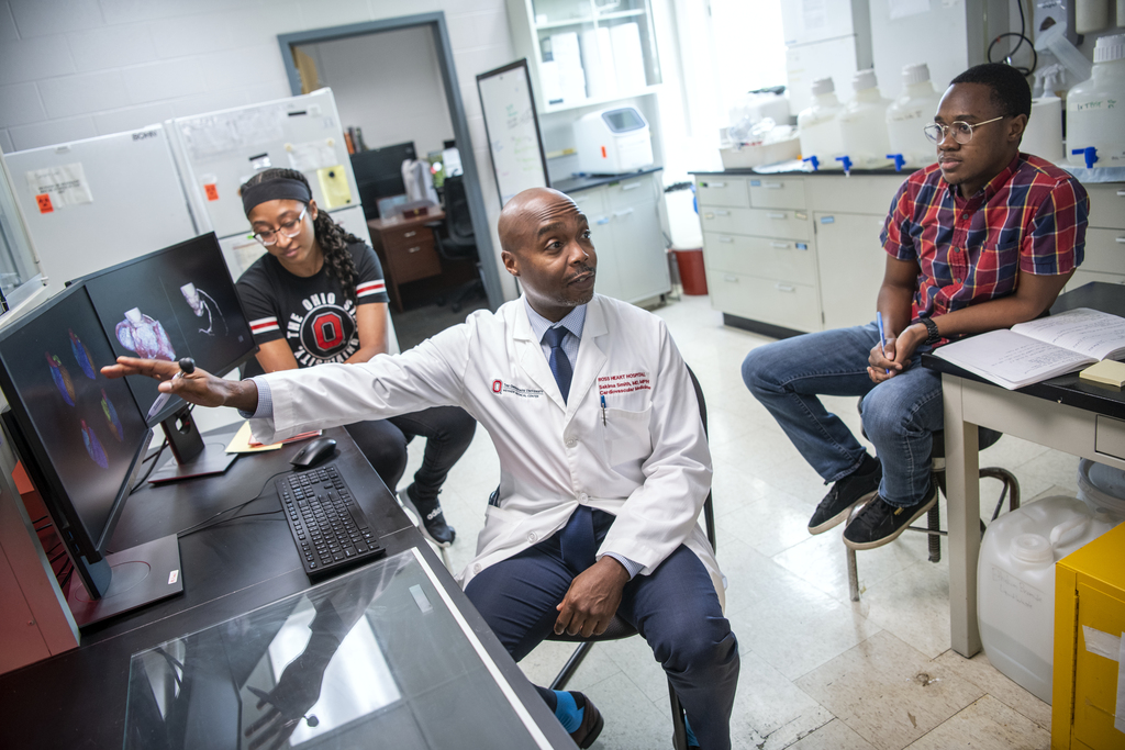 A clinical professor sits in front of a computer and explains something on screen to students.