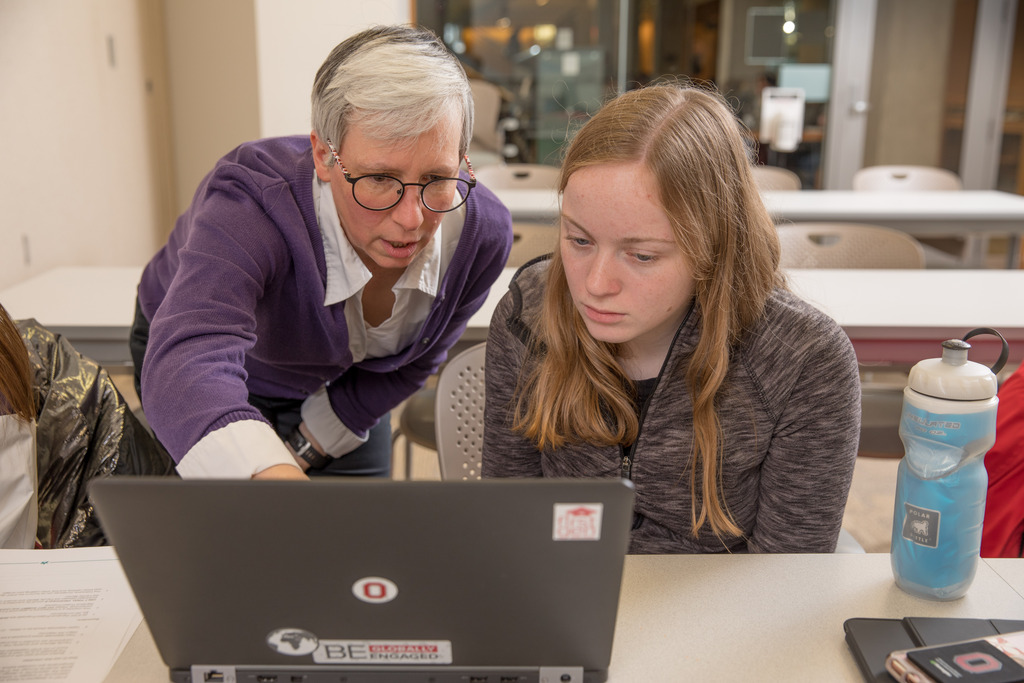 A professor stands over a student and explains a problem on a computer.