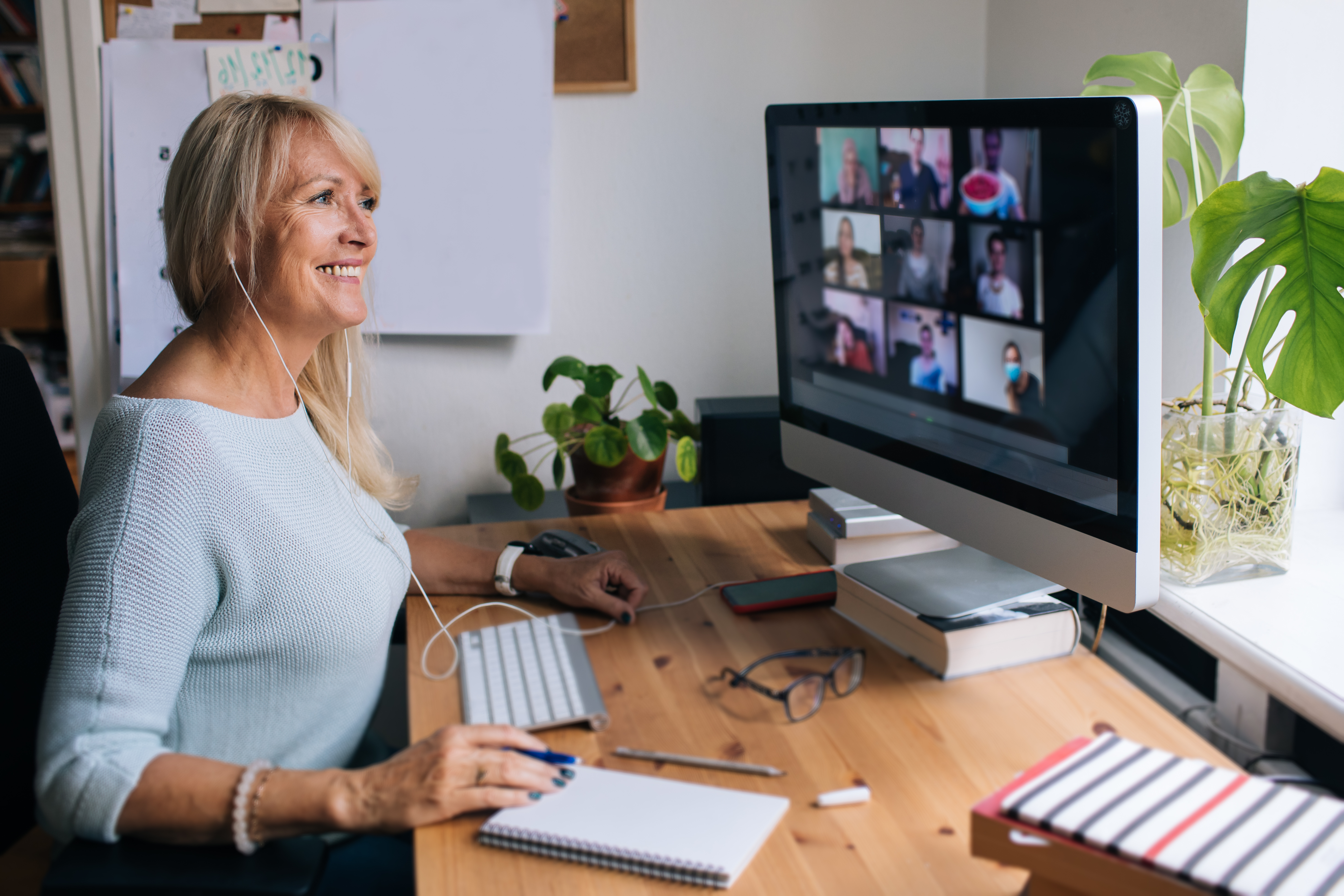 A smiling virtual event participant looks at a computer monitor showing a gallery of other attendees.