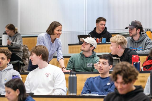 A professor speaks with seated students in a large lecture hall.