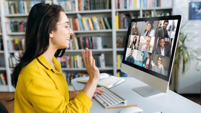 Smiling woman waves at fellow virtual workshop participants, seen on her computer monitor.