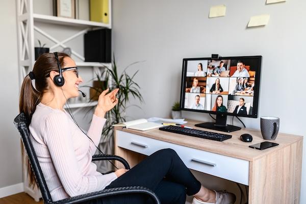 A person sits at a computer wearing headphones and speaking to virtual workshop participants that can be seen on the monitor.