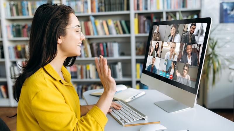 Smiling woman waves at fellow virtual workshop participants, seen on her computer monitor.