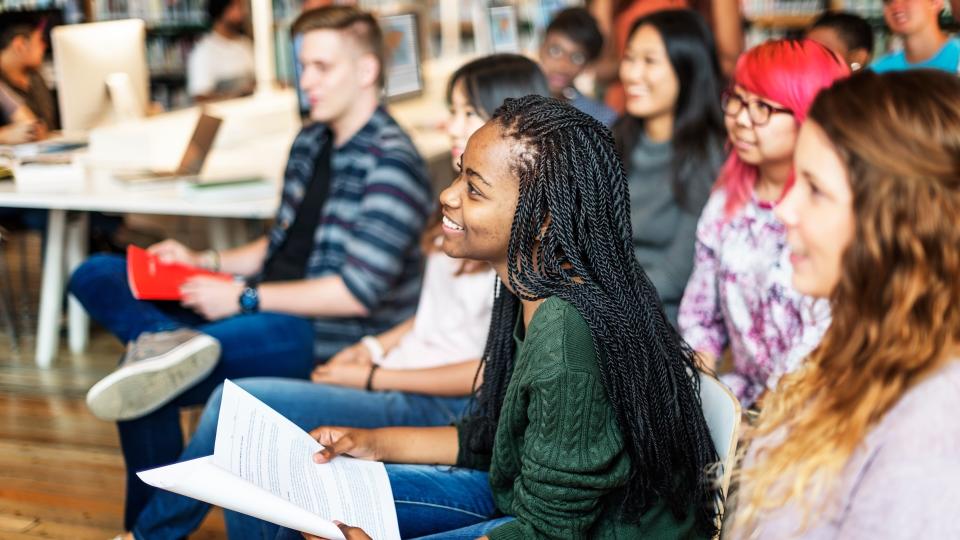Smiling students facing forward and attentively listening to an instructor who is not shown.