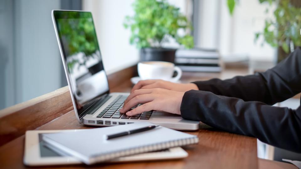 Hands typing on a laptop with a notepad nearby