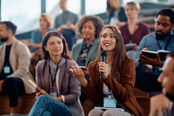 A smiling conference attendee holding a microphone asks a question.
