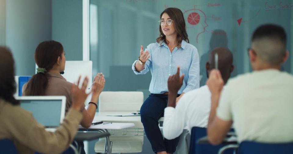 An instructor at the front of a class gestures to call on a student.