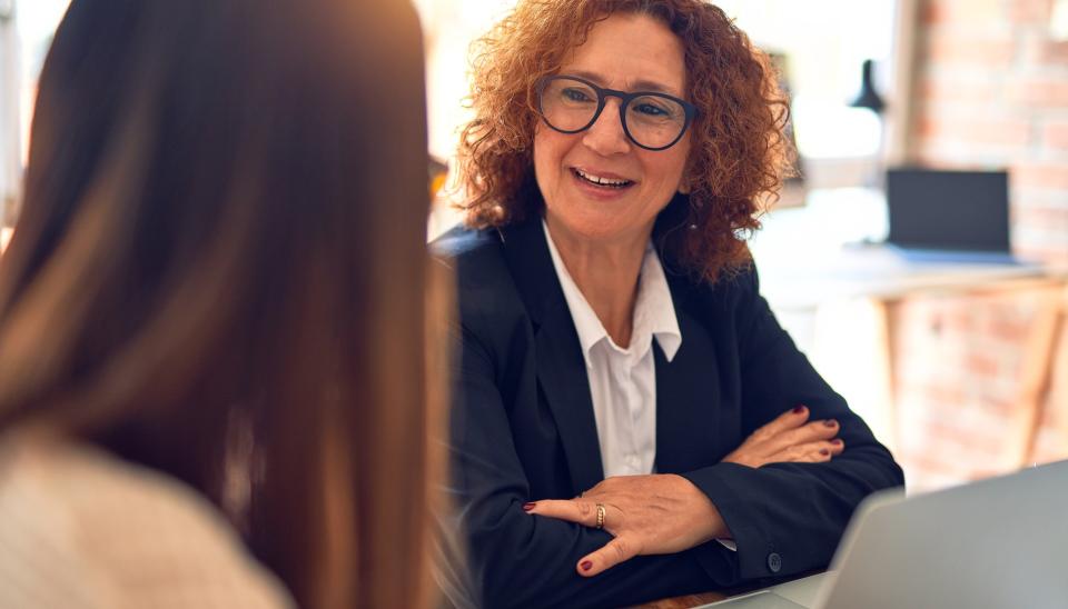 A smiling woman at a laptop speaks to a consultant.
