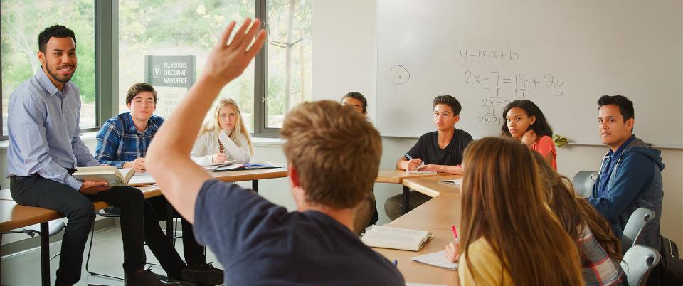 An instructor leading a class discussion looks at a student with a raised hand.