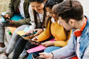 Several students on a bench looking at their devices