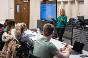 A faculty member presents on a television at the front of a small classroom.