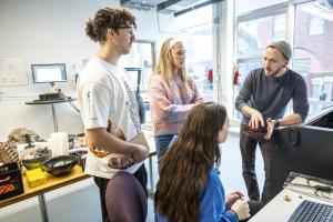 Four students huddle and talk in a small office.